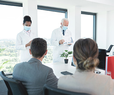 Two physicians are standing and showing reports to two people