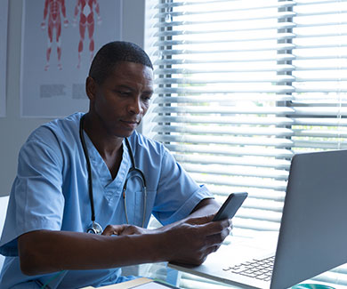 Doctor using mobile phone with computer in front of him at desk in hospital