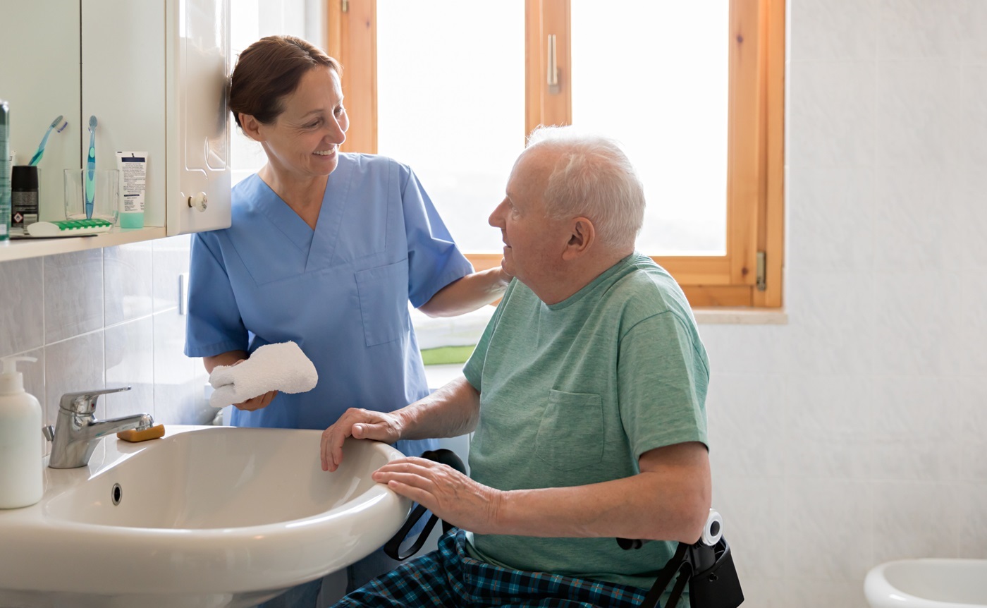 Nursing staff assist an elderly man washing at a sink
