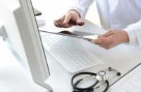 Doctor using a tablet in front of a laptop with a stethoscope