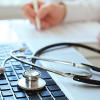 Stethoscope on a keyboard with a doctor writing in the background