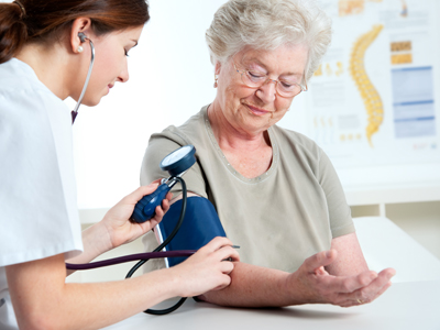 An older adult woman gets her blood pressure taken at the doctor’s office.