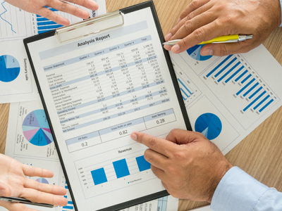 Hands pointing to a clipboard and sheets of paper showing numbers and charts.